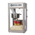 Stainless steel kettle corn popcorn machine with a glass enclosure, featuring a metal popping kettle above freshly popped popcorn and two red popcorn cups inside.