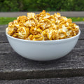 White bowl filled with pumpkin spice latte popcorn on a wooden surface with a blurred green background
