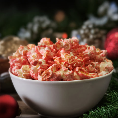 Bowl of red and white candy cane flavored popcorn surrounded by ornaments and garland.