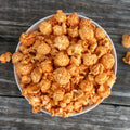 Top-down view of a white bowl filled with orange-seasoned popcorn on a wooden surface.