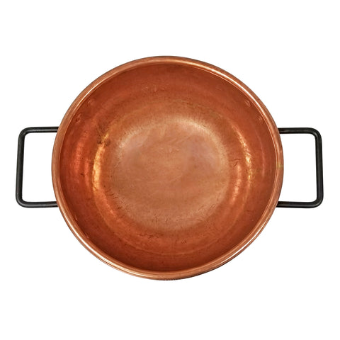 Overhead view of copper kettle with two black handles.